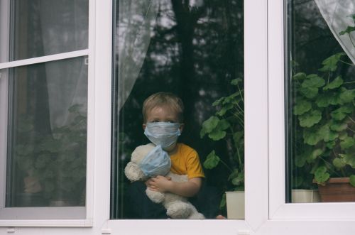 Sad child and his teddy bear look out window.
